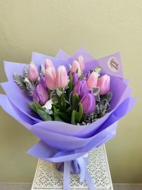 Bouquet of pink and lavender tulips with dusty miller foliage, wrapped in lilac paper with matching ribbon