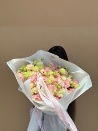 Bouquet of peach lisianthus flowers wrapped in white, held by a woman in a white blouse with long dark hair.