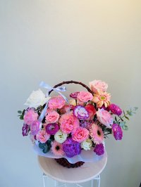 A vibrant bouquet of pink roses, white lilies, and purple orchids in a decorative basket.