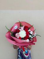 Person holding Betty bouquet with red and pink roses, white chrysanthemums, baby's breath and evergreen sprigs wrapped in pink paper
