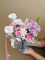 A bouquet of pink roses, white lilies, and purple orchids in a silver vase with pink ribbons.