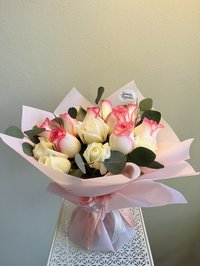 Bouquet of pink and white roses wrapped in pink paper with green foliage