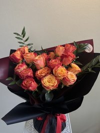 Bouquet of vibrant orange and red roses wrapped in dark paper with lush greenery