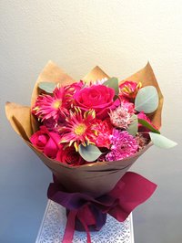A vibrant bouquet with pink roses, lilies, and orchids wrapped in brown paper