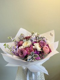 A bouquet of pink, white, and purple roses, lilies, and orchids wrapped in white paper.