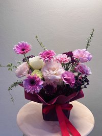 A bouquet of pink, white, and purple flowers with roses, lilies, and orchids, wrapped in a pink ribbon.
