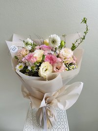 A bouquet of pink, white, and purple flowers including roses, lilies, and orchids wrapped in elegant paper.