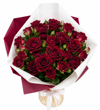 Bouquet of velvety red roses with green foliage wrapped in elegant paper