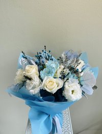Bouquet of white roses and blue lilies wrapped in blue paper
