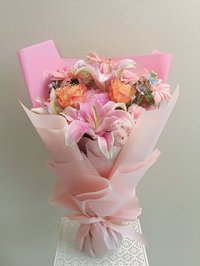 A bouquet of pink lilies, peach roses, and white orchids wrapped in soft pink paper.