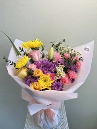 Bouquet with pink roses, white lilies, and purple orchids wrapped in elegant paper