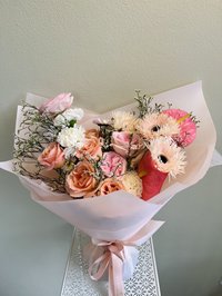 Pink and white bouquet with roses, lilies, and orchids wrapped elegantly in soft paper.