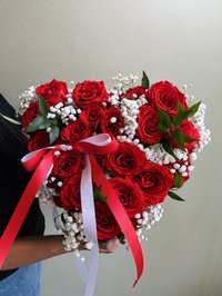 Heart-shaped bouquet of red roses and baby's breath with green leaves and red and white ribbons