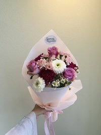 Pink, white, and purple flower bouquet with roses, lilies, and orchids wrapped in soft pink paper.