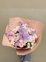 Bouquet of pink roses, white lilies, and purple orchids wrapped in peach paper.