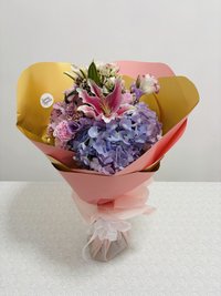 Pink, white, and purple bouquet with roses, lilies, and orchids wrapped in pink and gold paper.