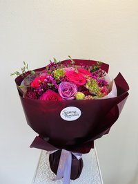 A vibrant bouquet of pink, white, and purple flowers with roses, lilies, and orchids in elegant wrapping.