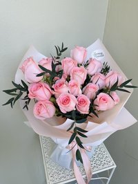 Bouquet of soft pink roses wrapped in white paper with greenery