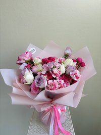 A bouquet of pink, white, and purple flowers including roses, lilies, and orchids, wrapped in pink paper with ribbons.