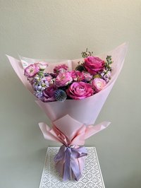 Beautiful bouquet with pink roses, white lilies, and purple orchids wrapped in soft pink paper with a lavender ribbon.