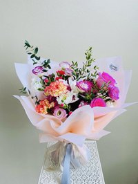 A bouquet of pink roses, white lilies, and purple orchids wrapped elegantly with foliage.