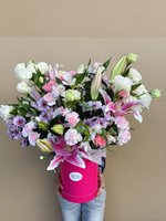 A vibrant bouquet of pink lilies, white roses, and purple orchids in a pink container.