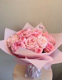A bouquet of pink roses wrapped in soft pink paper with a silver ribbon.