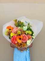 Vibrant bouquet with orange gerberas, pink roses, and yellow flowers wrapped in white paper