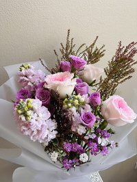 Bouquet of pink and purple roses with white lilies and orchids, wrapped in white paper