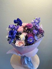 A bouquet of pink roses, purple lilies, and white orchids wrapped in pink paper with a blue ribbon.