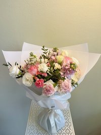 Bouquet of pink roses, white lilies, and purple orchids wrapped in white paper with a silver ribbon