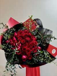 A large bouquet of red roses surrounded by lush greenery, wrapped in dark foliage.
