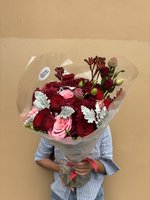 Bouquet of red and pink roses with greenery wrapped in clear cellophane.