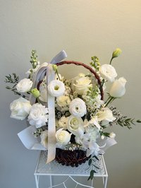A bouquet of white roses, lilies, and orchids in a wicker basket with a ribbon