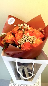 Bouquet of orange roses with white wax flowers in a decorative wrap.