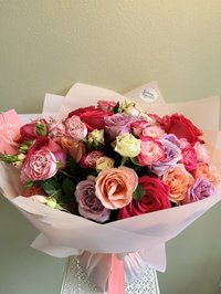 Bouquet of pink, white, and purple roses, lilies, and orchids wrapped in soft pink paper