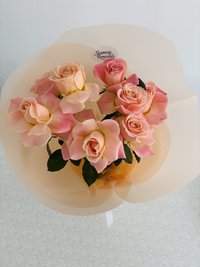 Bouquet of peach roses with delicate pink accents in elegant wrapping.