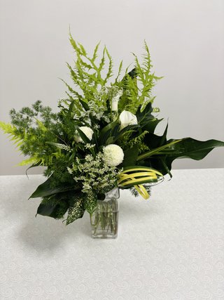 Asymmetrical Green Magic arrangement with white anthuriums, white chrysanthemums, layered green foliage, and a clear glass vase.