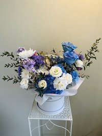 Blue and white rose bouquet with purple accents in a white round box on a decorative stand