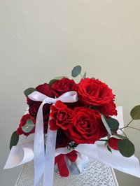Vibrant red rose bouquet with white ribbon and greenery.