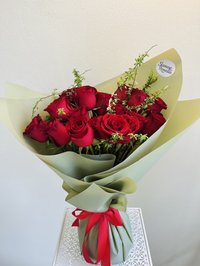 Bouquet of deep red roses with green foliage wrapped in elegant paper and tied with a red ribbon