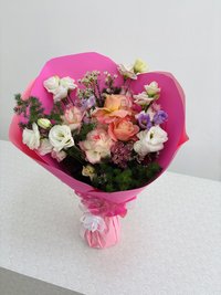 Pink, white, and purple bouquet with roses, lilies, and orchids wrapped in pink paper.