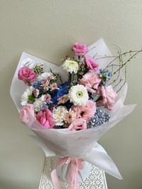 A bouquet of pink roses, white lilies, and purple orchids wrapped in elegant paper