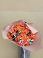 Bouquet of orange roses and coral carnations wrapped in peach paper
