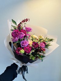 Bouquet of pink and purple roses, white lilies, and orchids wrapped in soft paper